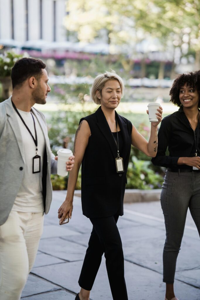 Three diverse business professionals walking and holding coffee outdoors, exhibiting teamwork and networking.